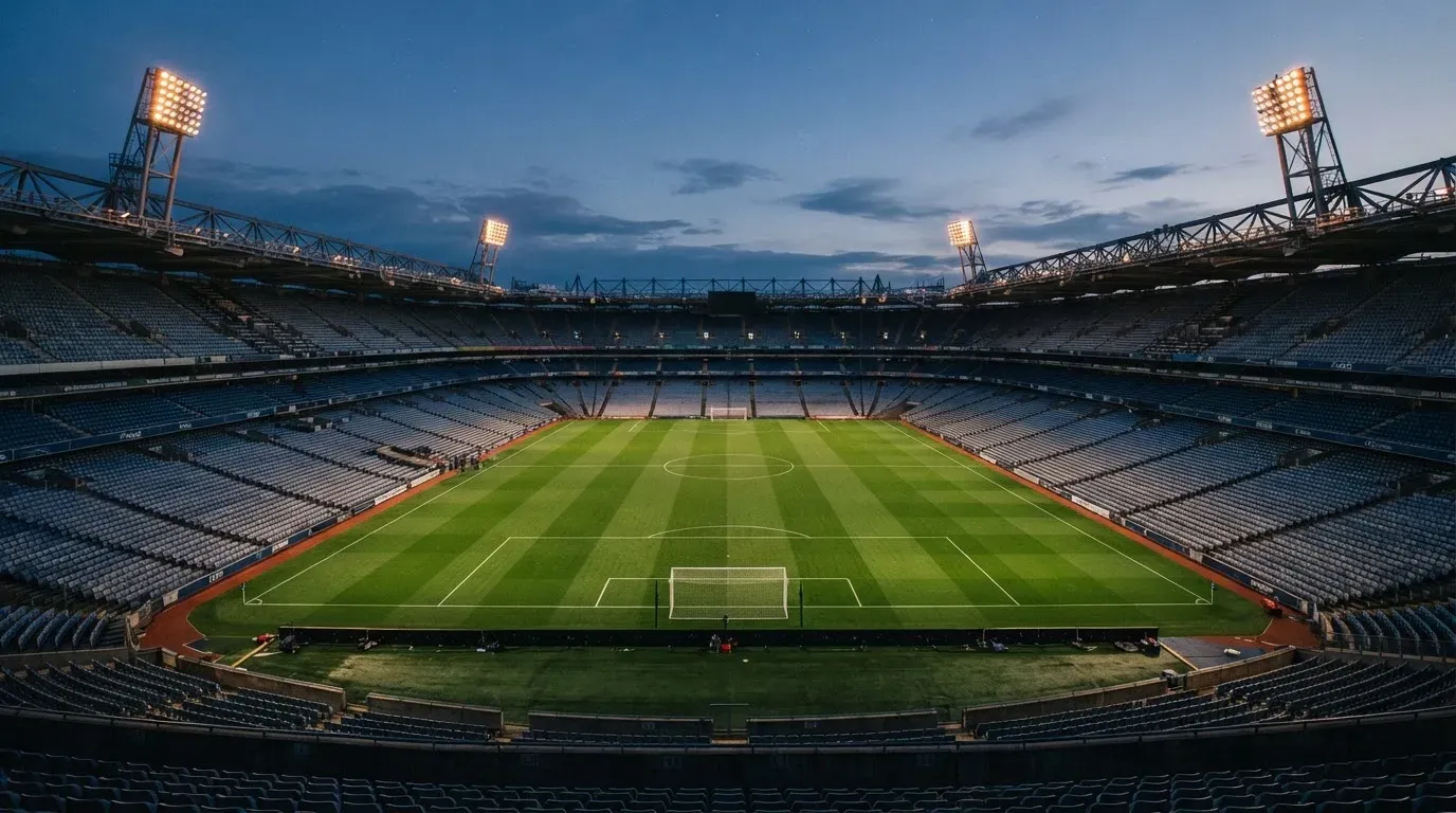 An empty football stadium with floodlight masts at dusk