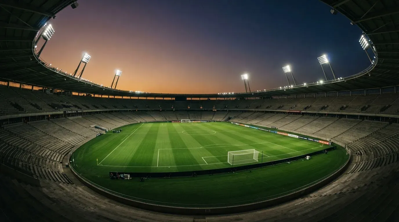 An empty football stadium with floodlight masts at dusk