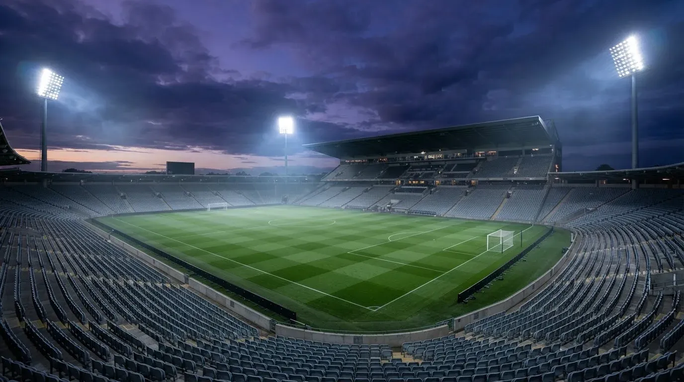 An empty football stadium with floodlight masts at dusk