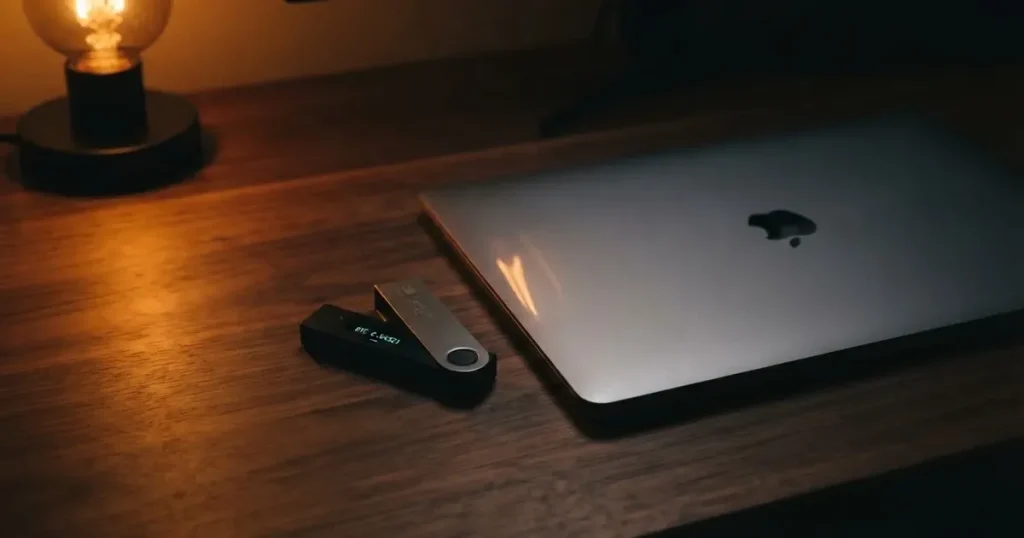 A hardware wallet and a closed laptop on a desk in dim light