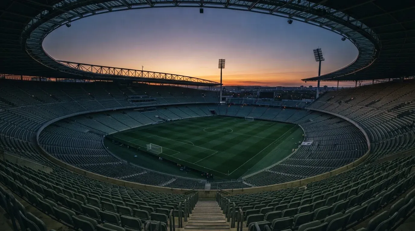 An empty football stadium with floodlight masts at dusk