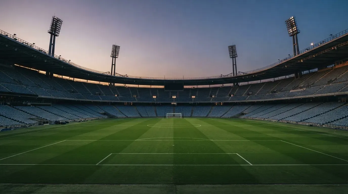 An empty football stadium with floodlight masts at dusk