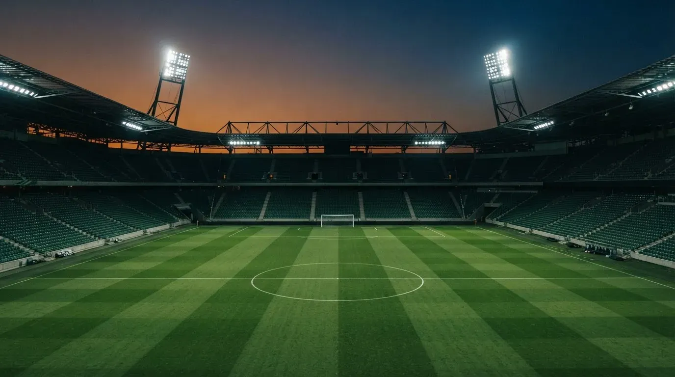 An empty football stadium with floodlight masts at dusk